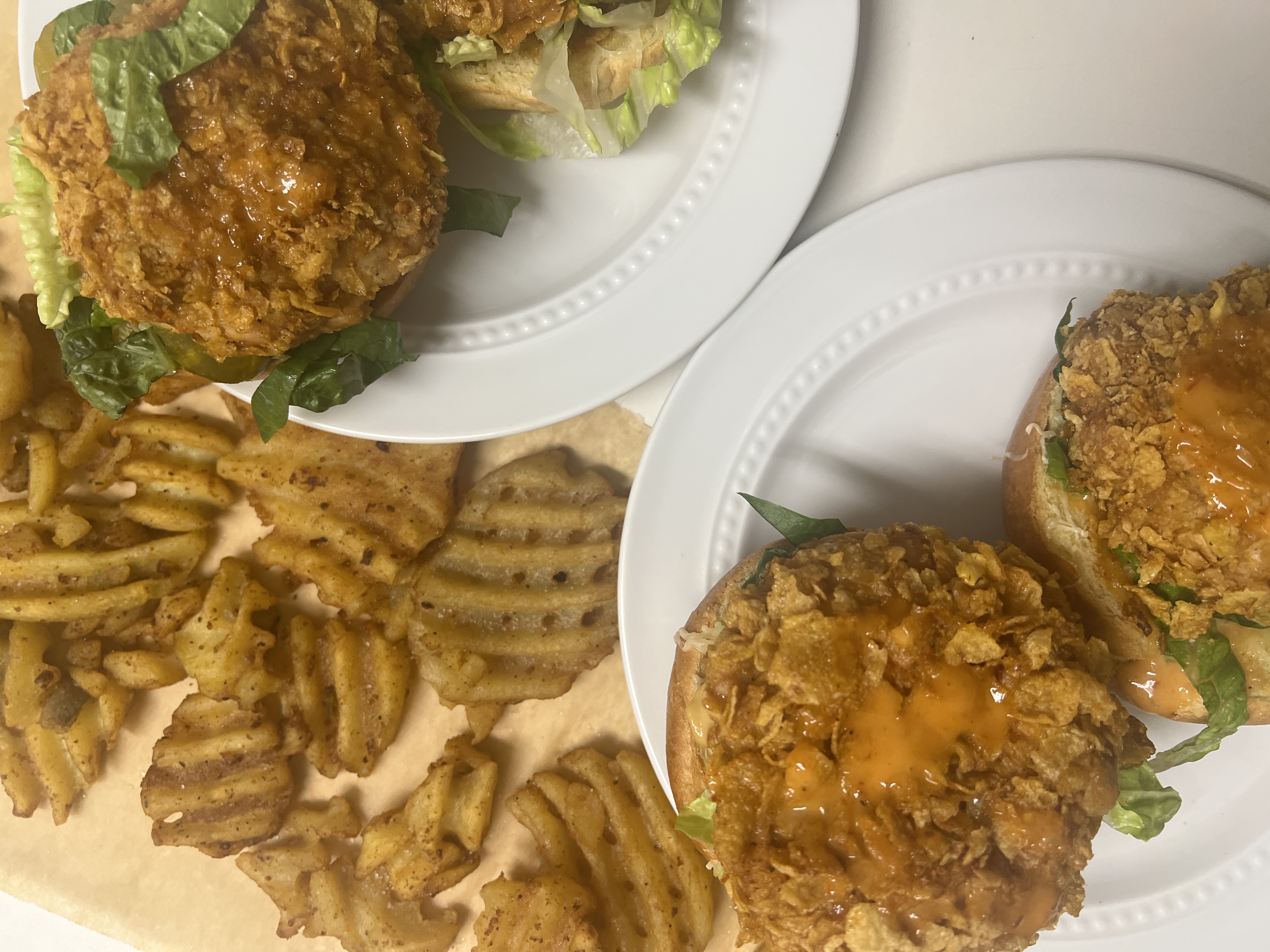 A scrumptious fried chicken patty on a bed of fresh lettuce, on a lightly toasted bun topped with barbecue sauce, served with a side of crispy waffle fries